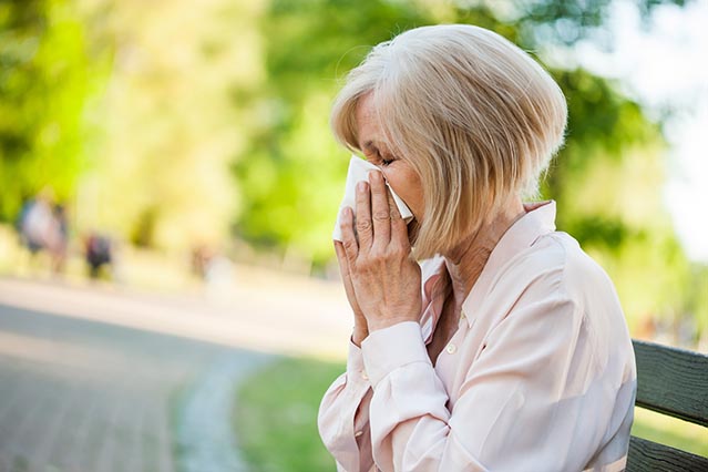 Woman sitting outside with allergies using kleenex